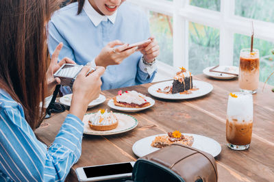 Midsection of women photographing food while sitting on table at restaurant