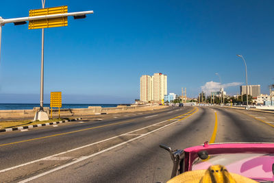 Road by buildings against clear blue sky