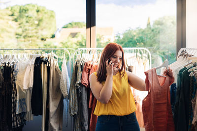 Young woman talking on phone while choosing dress at store