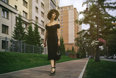 A pretty charming middle-aged woman in a black dress, hat and sunglasses strolls through the city 