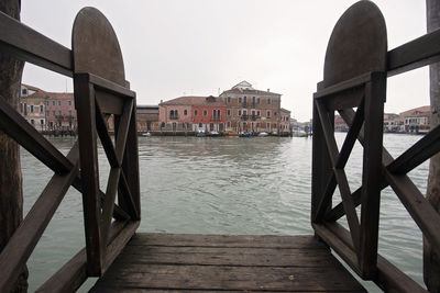 Wooden posts in canal amidst buildings against sky