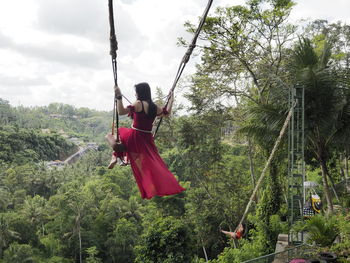 Rear view of woman sitting on swing against trees