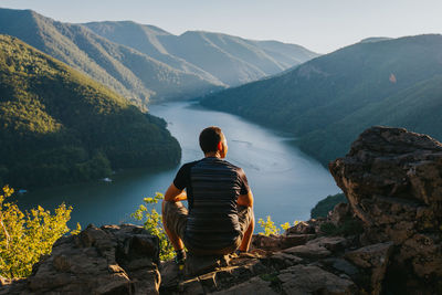 Rear view of man sitting on rock looking at mountains