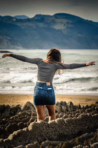 Rear view of woman with arms outstretched standing on beach