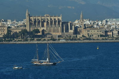 Sailboats sailing on sea by buildings in city