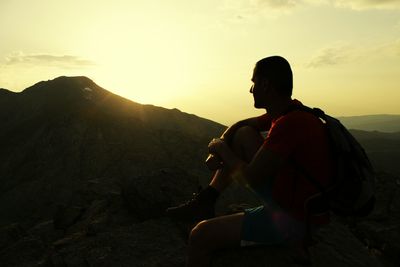 Hiker sitting on cliff against sky during sunset