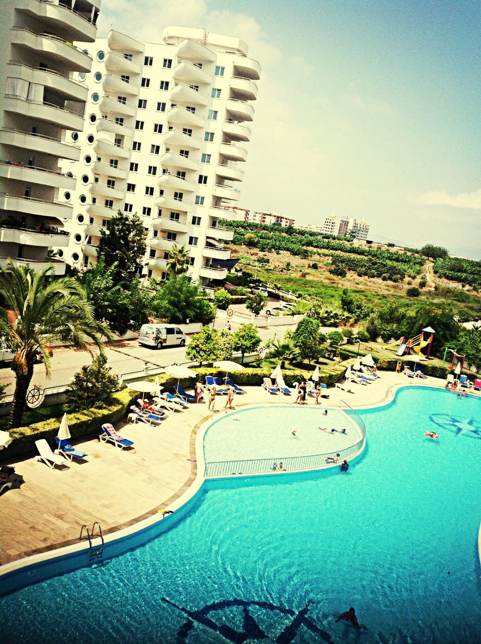 building exterior, architecture, built structure, city, water, tree, palm tree, blue, sky, sea, incidental people, beach, swimming pool, high angle view, building, day, tall - high, skyscraper, cityscape, residential building