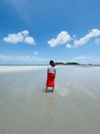 Rear view of woman standing at beach against sky