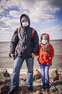 Father and daughter wearing respirator masks staying together on the empty bank of sea