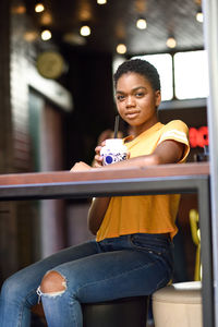 Portrait of young woman sitting on chair at restaurant