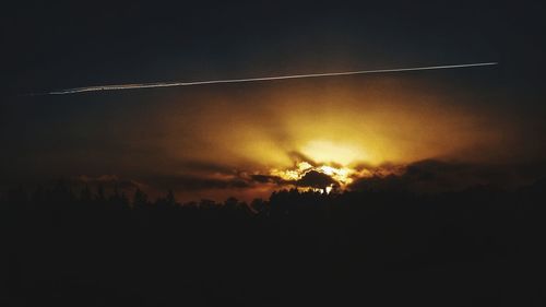 Low angle view of silhouette vapor trail against sky during sunset