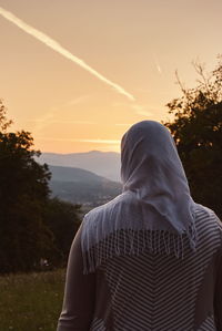 Rear view of woman standing against sky during sunset