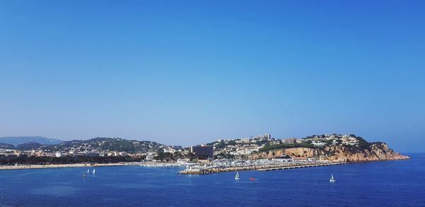 Scenic view of sea by buildings against clear blue sky