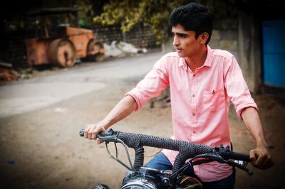 Young man looking away while riding bicycle on road