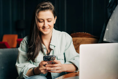 A young brunette woman sits in a cafe and surfs the internet using a mobile phone.