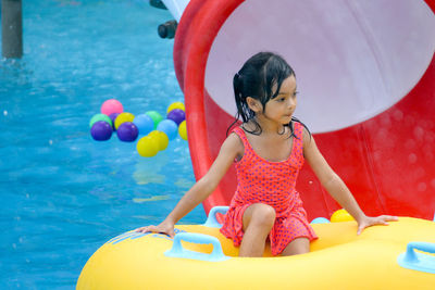 Cute girl looking away while sitting in inflatable ring on swimming pool