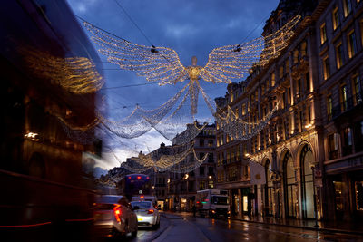 Illuminated street amidst buildings against sky in city