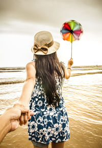 Cropped image of boyfriend holding girlfriend hand at beach against sky