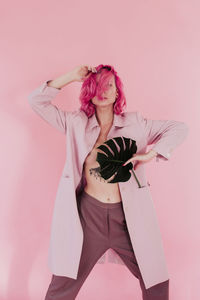 Young woman with dyed hair holding leaf while standing against colored background