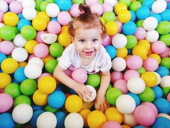 High angle portrait of girl sitting amidst multi colored balls