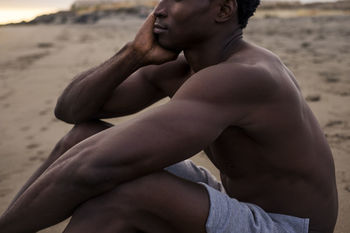 Midsection of man sitting at beach during sunset