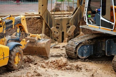 A yellow digger excavating mud and one crane bucket picking up