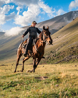 Rear view of a caucasian girl on a horse gallops through a mountain valley against sky