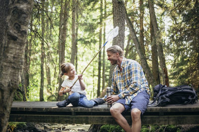 Smiling daughter sprinkling water on father through fishing net in forest