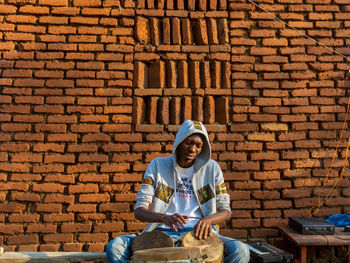 Full length of young man sitting against brick wall