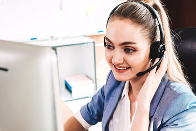 Smiling businesswoman wearing headset looking at computer on desk in office