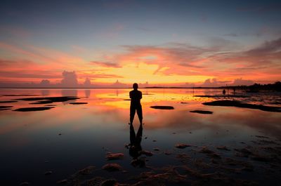 Silhouette man standing on beach against sky during sunset