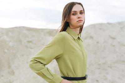 Fashion beauty portrait of young woman with long hair in green organic suit on the desert background