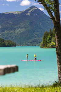 Man and woman paddleboarding on lake by mountain