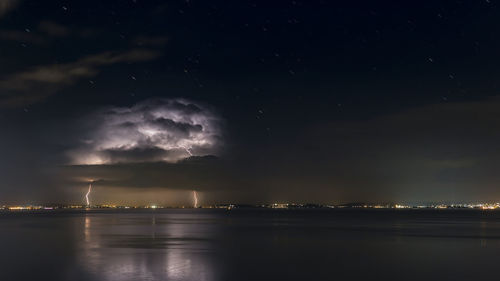 Scenic view of sea with lighting against sky at night