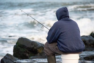 Rear view of man fishing at shore