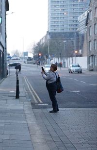 Side view of woman photographing on street in city