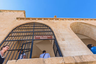 Low angle view of people walking on building against blue sky