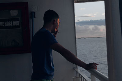 Side view of young man smoking by railing in ship