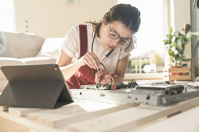 Young woman working on computer equipment at home next to tablet