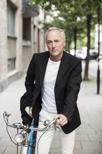 Portrait of confident businessman with bicycle standing on sidewalk