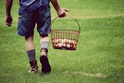 Low section of farmer man wearing shoes on grass carrying egg basket