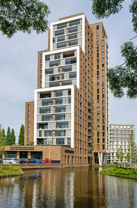 The brick, wood and glass facades of the bankras residential tower reflecting in the adjacent pond