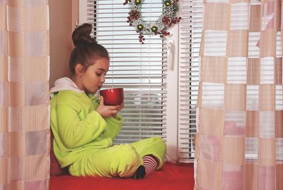 Girl having coffee while sitting on window sill