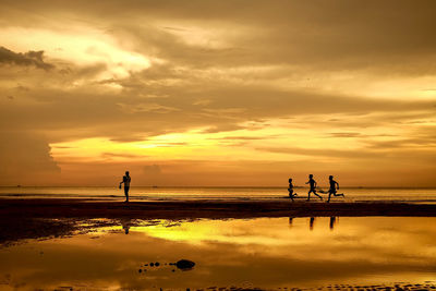 Silhouette people on beach against sky during sunset