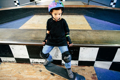 Young boy sits with his skateboard in an indoor skatepark