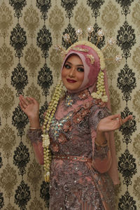 Portrait of a smiling young woman standing against wall