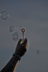 Low angle view of hand holding bubbles against sky
