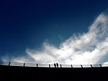 Low angle view silhouette of people on bridge against blue sky