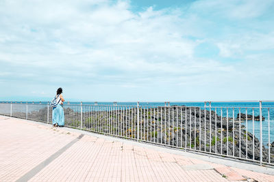 Rear view of man standing by railing against sky