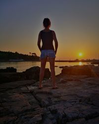 Rear view of man standing on rock at beach during sunset